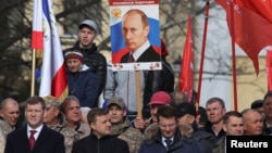 A man holds a board with a portrait of Russian President Vladimir Putin during celebrations of the fifth anniversary of Russia's annexation of Crimea in Simferopol, Crimea, March 15, 2019. 