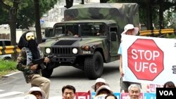 Warga Korsel memprotes latihan militer bersama AS-Korsel di Seongnam, bagian Selatan Korea Selatan, sementara kendaraan militer AS melaju di dekatnya (16/8)