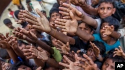 Rohingya Muslim children, who crossed over from Myanmar into Bangladesh, stretch their arms out to collect chocolates and milk distributed by Bangladeshi men at Taiy Khali refugee camp, Bangladesh, Sept. 21, 2017.