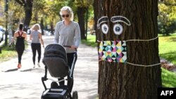 A woman pushes a pram past a giant mask and eye display stuck to a tree in Melbourne, May 8, 2020, as Australia's government unveiled a three-stage plan to get the economy back to a new normal by the end of July. 
