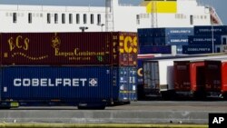 Truck trailers are parked among stacked cargo containers at the Port of Zeebrugge, in Zeebrugge, Belgium, Thursday, Oct. 24, 2019.  British police raided two sites in Northern Ireland and questioned a truck driver as they investigate the deaths of…