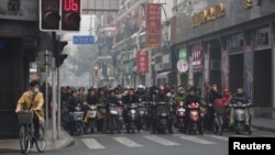 Local residents wait on motorcycles and bicycles at a traffic junction during a hazy day in downtown Shanghai, China, Dec. 6, 2013. 