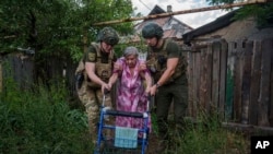 Agentes de la unidad de policía Ángeles Blancos ayudan a una mujer mayor a llegar a una camioneta durante una evacuación, en Toretsk, en la región ucraniana de Donetsk, el 28 de junio de 2024. 