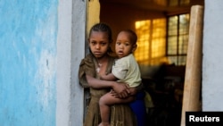 FILE - An 11-year-old girl holds her year-old brother at the doorway to a classroom now used as living space at the Tsehaye primary school, which housed people displaced by conflict, in Shire, Tigray region, Ethiopia, March 15, 2021.