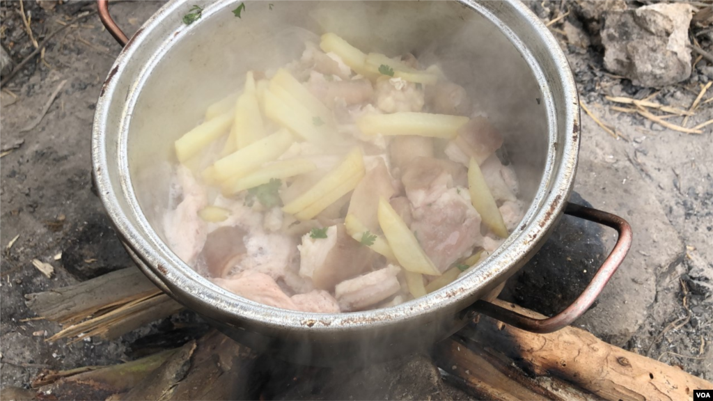 Un grupo de venezolanos cocina papa con pollo al lado de la carretera aledaña a la frontera. Los alimentos son donados por colombianos que viven en el área. Ipiales, Colombia, 11 de septiembre de 2019. Foto: Celia Mendoza - VOA.