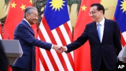 Malaysian Prime Minister Mahathir Mohamad, left, shakes hands with his Chinese counterpart Li Keqiang at the end of a press conference at the Great Hall of the People in Beijing, Aug. 20, 2018. 