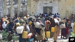 Somalis carrying their belongings wait outside an internally displaced camp in Mogadishu, Somalia, after they fleeing from southern Somalia due to lack of food and water, July 5, 2011