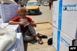 A girl drinks from a plastic bag of water as she sits atop a cart next to humanitarian aid packages provided by the United Nations Relief and Works Agency for Palestine Refugees in central Gaza City on Aug. 27, 2024.