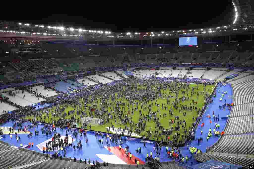 Espectadores correm para dentro do campo de futebol no Estádio de França depois de uma explosão perto do estádio, Nov. 13, 2015.