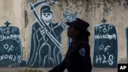 Una mujer policia camina frente a un mural pintado por las pandillas, durante un patrullaje en una zona de la capital salvadoreña controlada por las maras.