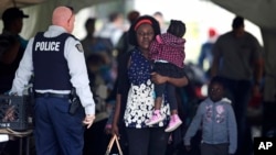 A woman carries a child out of a makeshift police station after crossing illegally into Canada, from the end of Roxham Road in Champlain, New York, in Saint-Bernard-de-Lacolle, Quebec, Aug. 7, 2017.