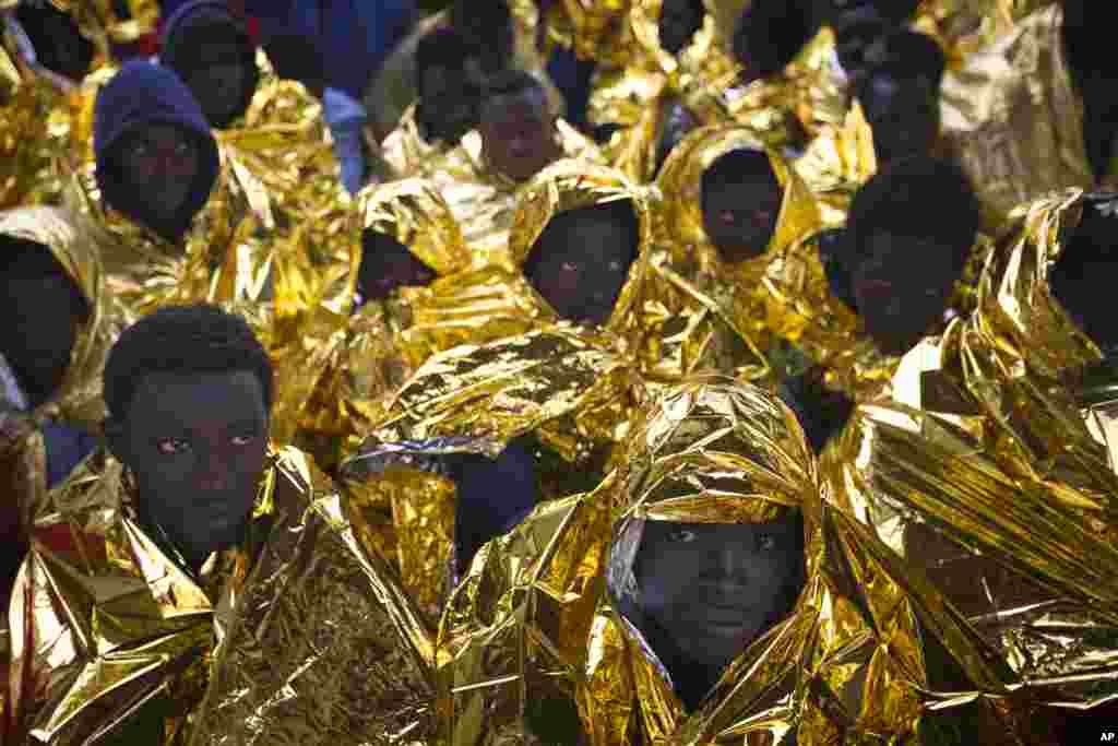 Wrapped in blankets, Sub-Saharan migrants sit on the deck of the Golfo Azzurro rescue vessel after arriving at the port of Messina, in Italy, with more than 299 migrants aboard the ship rescued by members of Proactive Open Arms NGO.