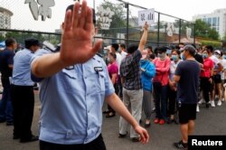 A police officer gestures at a photographer as people line up to get a nucleic acid test at a sport center after a spike of cases of the coronavirus disease (COVID-19), in Beijing, China June 17, 2020. REUTERS/Thomas Peter