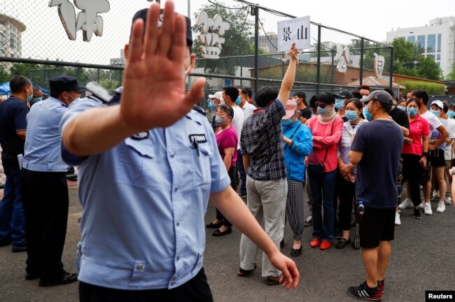 A police officer gestures at a photographer as people line up to get a nucleic acid test at a sport center after a spike of cases of the coronavirus disease (COVID-19), in Beijing, China June 17, 2020. REUTERS/Thomas Peter