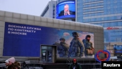 On a Moscow street, an image of Russian President Vladimir Putin is displayed on the facade of a building behind an electronic board promoting contract military service in the Russian army, Dec. 19, 2024. 