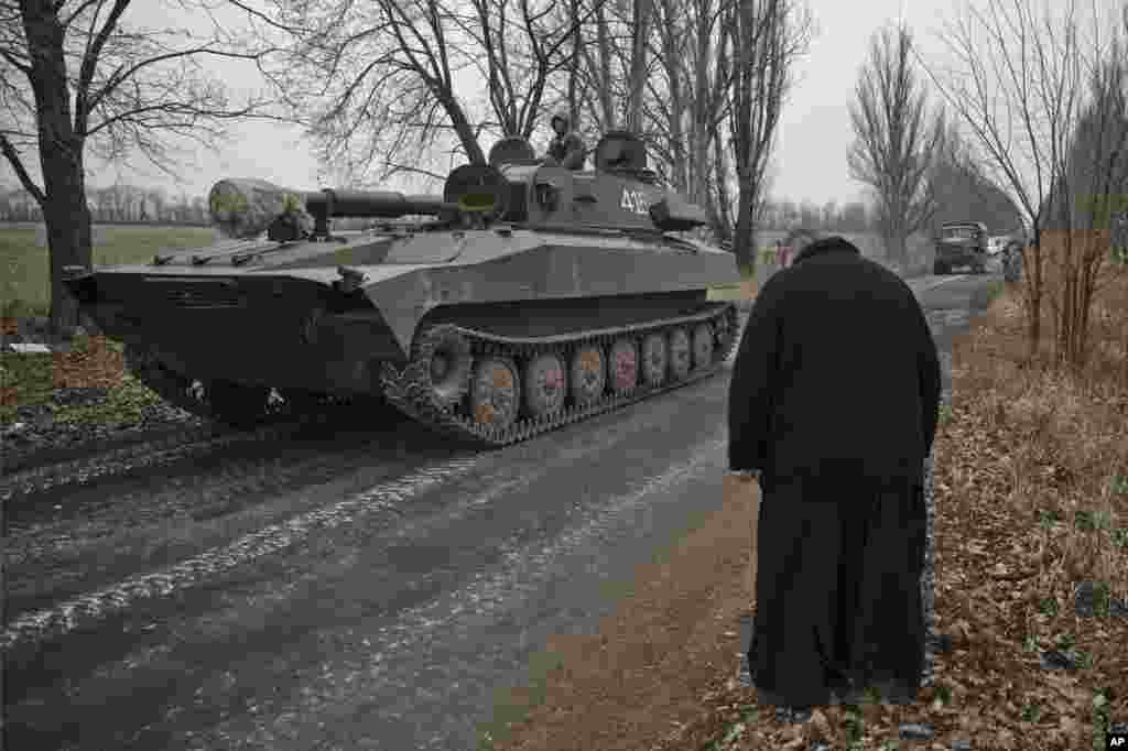 A priest bows as Russia-backed separatist fighters drive in a self-propelled 152 mm artillery piece, part of a unit that was moved away from the front lines, in Yelenovka, near Donetsk, Feb. 26, 2015.