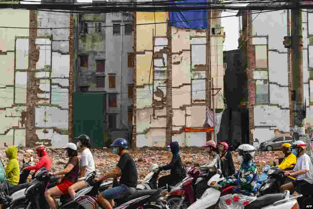 Drivers ride their vehicles past a living area being cleared for road expansion in Hanoi, Vietnam.
