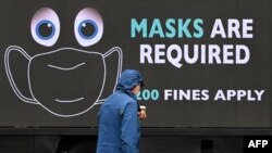 Seorang pria berjalan melewati truk bertuliskan peringatan untuk mengenakan masker di Melbourne, 5 Agustus 2020 di tengah pandemi Covid-19. (Foto: William WEST / AFP)