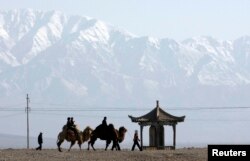 FILE - Visitors ride camels outside the Jiayuguan Pass Town in front of the snow-covered Qilian Mountains in Jiayuguan, northwest China's Gansu province April 28, 2007. REUTERS/Jason Lee