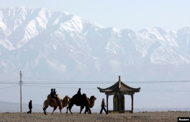 FILE - Visitors ride camels outside the Jiayuguan Pass Town in front of the snow-covered Qilian Mountains in Jiayuguan, northwest China's Gansu province April 28, 2007. REUTERS/Jason Lee