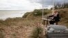 World War II D-Day veteran and Penobscot Elder from Maine, Charles Norman Shay sits on a bench next to his memorial stone at Omaha Beach prior to a ceremony in Saint-Laurent-sur-Mer, Normandy, France, Friday June 5, 2020.