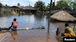 People sit in front of a submerged building in the Patani community in Nigeria's Delta state, which was hit by severe floods in the past few weeks, October 15, 2012.
