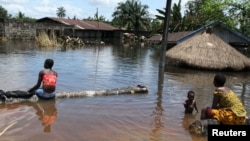 People sit in front of a submerged building in the Patani community in Nigeria's Delta state, which was recently hit by severe floods, October 15, 2012.