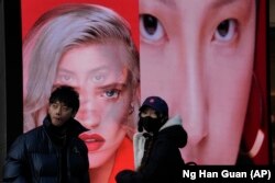 Seorang perempuan yang mengenakan masker berdiri di dekat sebuah papan iklan yang menampilkan model untuk produk kecantikan di Beijing, China, pada 28 Desember 2021. (Foto: AP/Ng Han Guan)