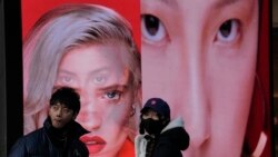 Seorang perempuan yang mengenakan masker berdiri di dekat sebuah papan iklan yang menampilkan model untuk produk kecantikan di Beijing, China, pada 28 Desember 2021. (Foto: AP/Ng Han Guan)