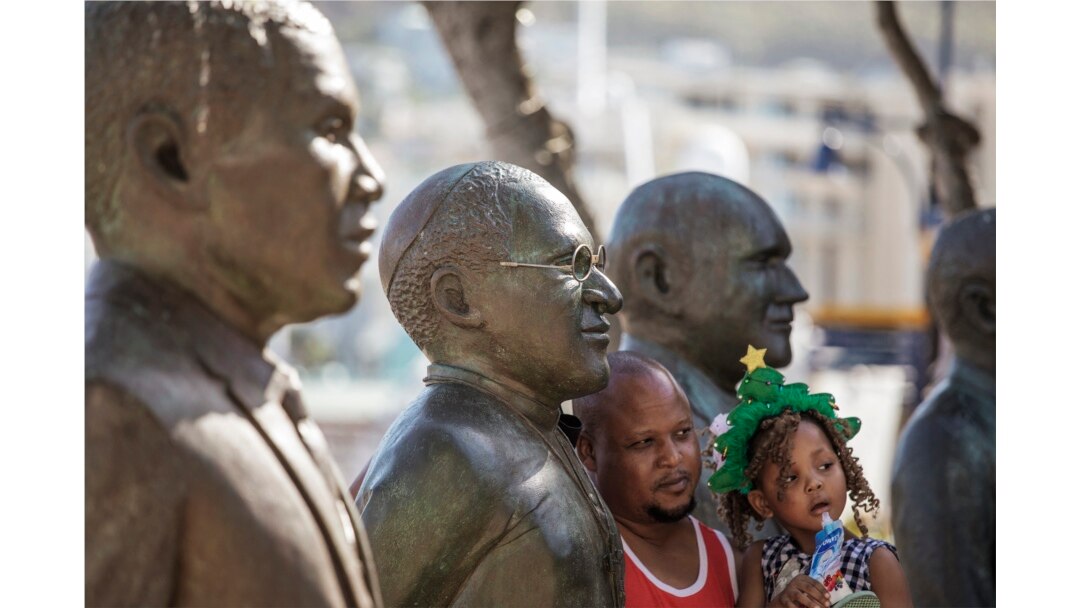 Seorang pria dan putrinya berpose dengan patung ikon anti-apartheid Afrika Selatan Uskup Agung Desmond Tutu setelah kematian Tutu di Victoria and ALbert Waterfront di Cape Town pada 26 Desember 2021. (Foto: AFP)