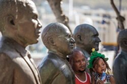 Seorang pria dan putrinya berpose dengan patung ikon anti-apartheid Afrika Selatan Uskup Agung Desmond Tutu setelah kematian Tutu di Victoria and ALbert Waterfront di Cape Town pada 26 Desember 2021. (Foto: AFP)