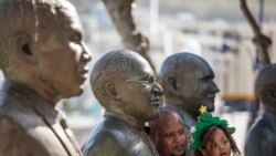A man and his daughter pose by South African anti-apartheid icon Archbishop Desmond Tutu's statue on the wake of Tutu's death at the Victoria and ALbert Waterfront in Cape Town on Dec. 26, 2021.