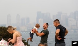 A man twirls a young child on a waterfront park as downtown Seattle disappears in a smoky haze behind, Aug. 19, 2018.