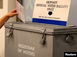 A ballot is placed into a locked ballot box by a poll worker as people line-up to vote early at the San Diego County Elections Office in San Diego, California, US, Nov. 7, 2016.