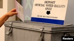 FILE - A ballot is placed into a locked ballot box by a poll worker as people line-up to vote early at the San Diego County Elections Office in San Diego, California, Nov. 7, 2016. 