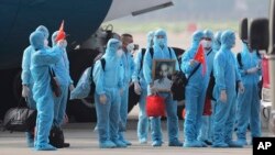 Vietnamese COVID-19 patients in protective gear, holding Vietnamese flags and carrying a portrait of the national leader Ho Chi Minh, arrive at the Noi Bai airport in Hanoi, Vietnam, on Wednesday, July 29, 2020. (Tran Huy Hung/VNA via AP)