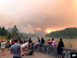 A photo provided by Inciweb shows people at a viewpoint overlooking the Columbia River watching the Eagle Creek wildfire burning in the Columbia River Gorge east of Portland, Oregon, Sept. 4, 2017.