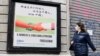 一名戴着口罩的妇女走过米兰街头一幅显示意大利与中国握手的广告牌。（2020年3月10日）