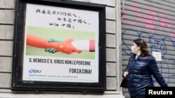 一名戴着口罩的妇女走过米兰街头一幅显示意大利与中国握手的广告牌。（2020年3月10日）