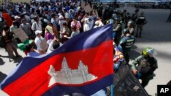 Supporters gather in front of riot police officers at a blocked main street near Phnom Penh Municipality Court in Phnom Penh, Cambodia, Wednesday, July 16, 2014. Five of lawmakers from the main opposition party of Cambodia National Rescue Party appeared in the court Wednesday for being questioned that they led about a hundred of their supporters on Tuesday to demonstrate in front of the park, asking authorities to open the site to the public. (AP Photo/Heng Sinith)