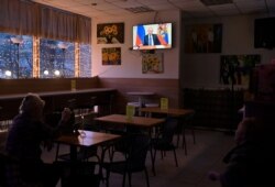 FILE - People watch a broadcast of Russian President Vladimir Putin's address to the nation on measures to combat the spread of the coronavirus, in a cafe in Omsk, Russia, March 25, 2020.