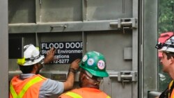 FILE - New York subway workers place a "flood door" decal onto steel doors, installed nearly five years after Superstorm Sandy flooding at South Ferry subway station, in New York on Tuesday June 27, 2017.