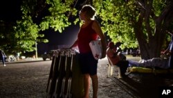 A woman holds a blanket and cots as neighbors remain outdoors using camping tents and portable lights for fear of possible aftershocks.