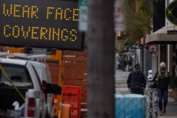 FILE - People walk past a sign warning to wear masks, in Encinitas, California, Jan. 25, 2021.