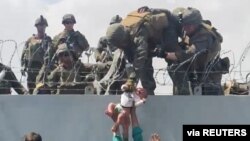 A baby is handed to U.S. soldiers over the perimeter wall of the airport for it to be evacuated, in Kabul, Afghanistan, Aug. 19, 2021, in this still image taken from video obtained from social media. 
