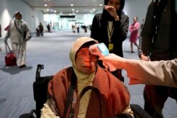 A health official scans the body temperature of a passenger as she arrives at the Soekarno-Hatta International Airport in Tangerang, Indonesia, Wednesday, Jan. 22, 2020. (AP Photo/Tatan Syuflana)