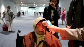 A health official scans the body temperature of a passenger as she arrives at the Soekarno-Hatta International Airport in Tangerang, Indonesia, Wednesday, Jan. 22, 2020. (AP Photo/Tatan Syuflana)