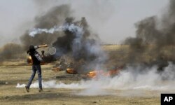 A Palestinian protester uses a tennis racquet to hit a teargas canister toward Israeli soldiers during a protest at the Gaza Strip's border with Israel, May 11, 2018.