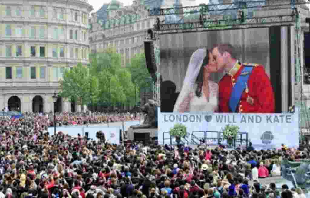 Royal supporters watch Britain's Prince William kissing his wife Kate, Duchess of Cambridge on a giant screen in Trafalgar Square in central London, after the wedding ceremony, on April 29, 2011.