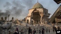 FILE - Iraqi civilians fleeing walk past the destroyed al-Nuri mosque as Iraqi forces continue their advance against Islamic State militants in the Old City of Mosul, Iraq, July 4, 2017.